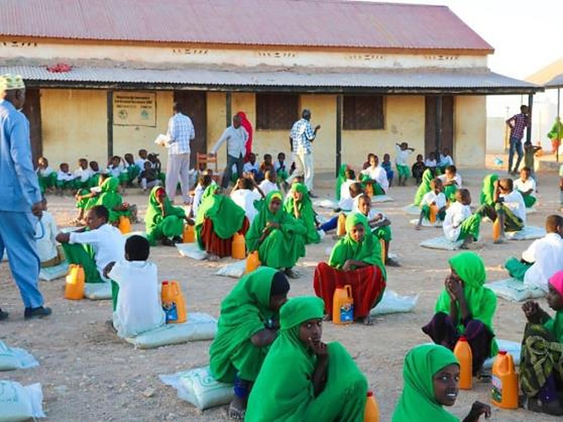 School pupils seated in a school yard with food rations
